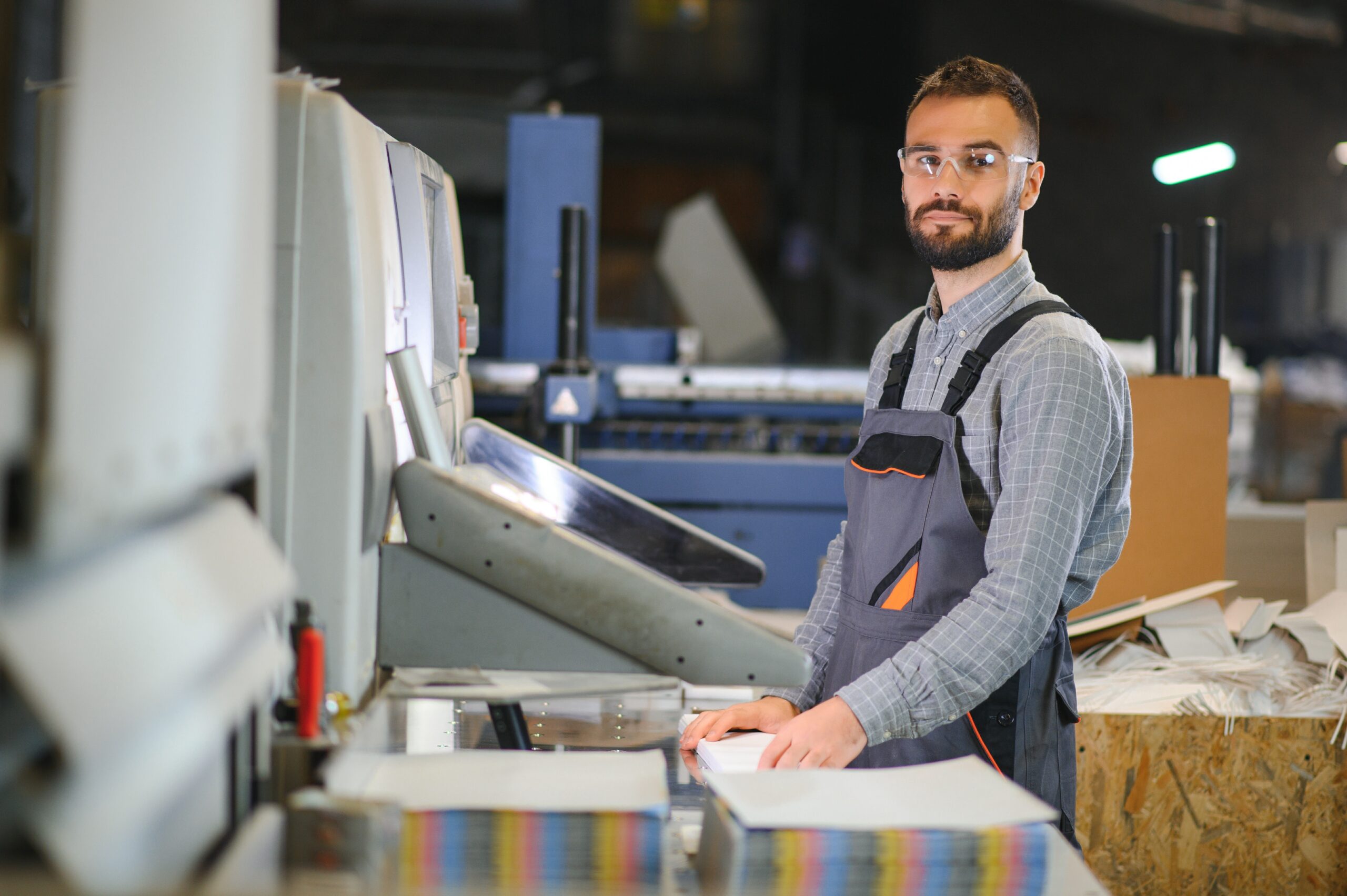 Printing house interior with modern offset print machine and operator in working uniform checking quality and controlling process of print Printing house interior with modern offset print machine and operator in working uniform checking quality and controlling process of print