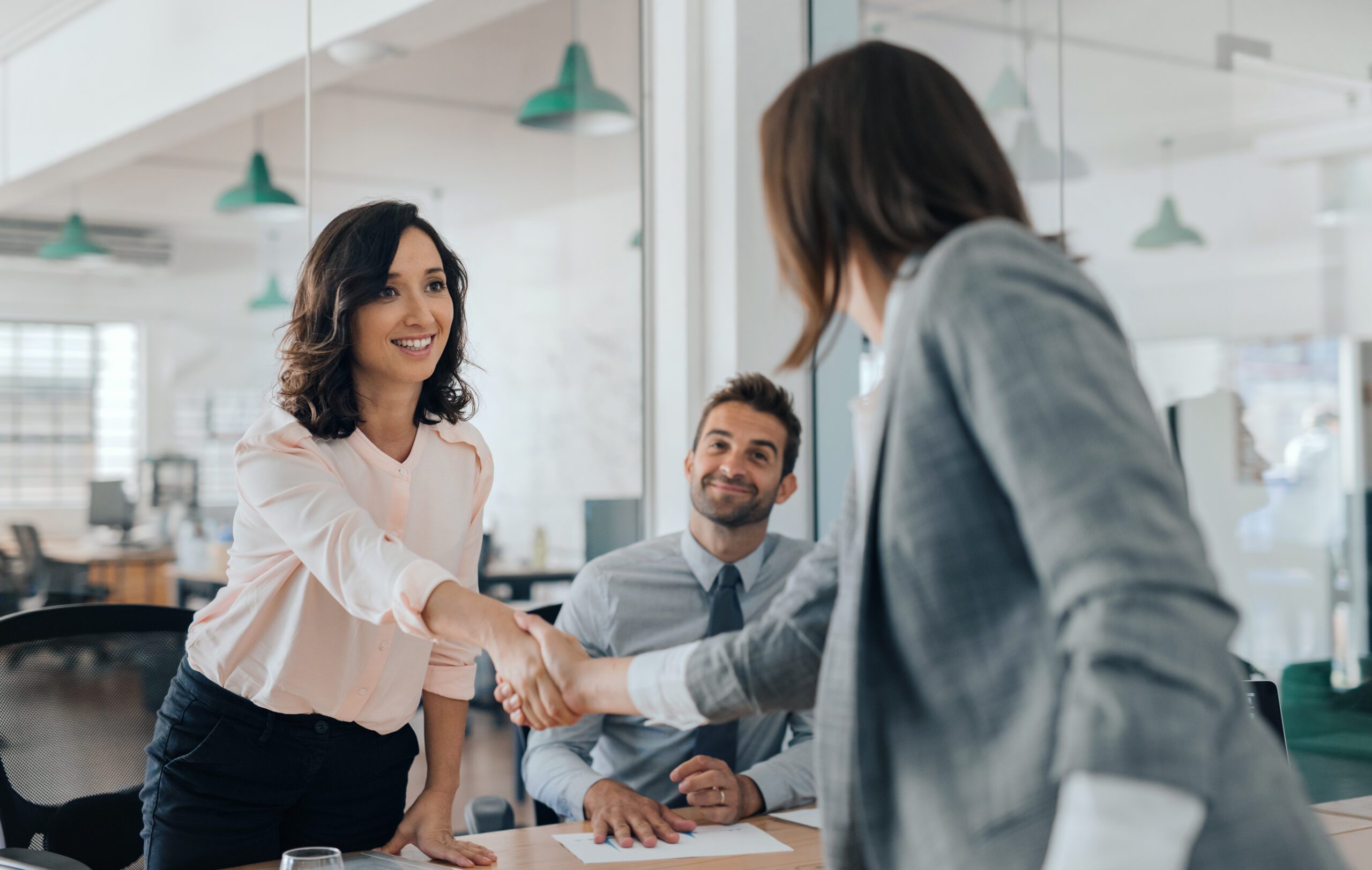 Smiling young businesswoman shaking hands with an office colleague Smiling young businesswoman shaking hands with an office colleague